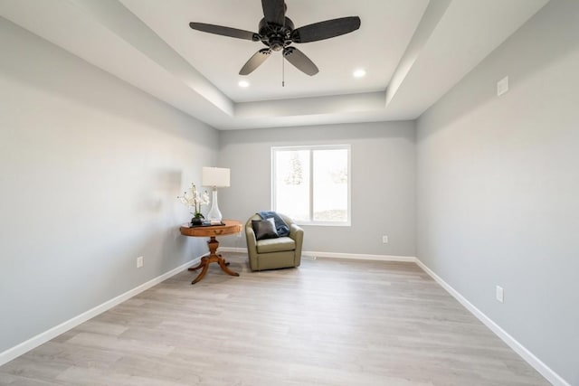 living area featuring a tray ceiling, baseboards, and light wood-style floors