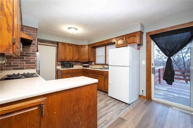 kitchen with light wood finished floors, brown cabinets, freestanding refrigerator, stainless steel microwave, and black electric stovetop