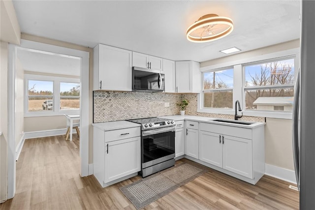 kitchen with stainless steel appliances, light wood finished floors, a sink, light countertops, and white cabinets