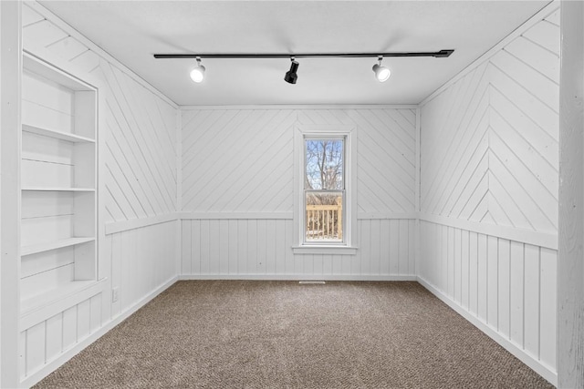 carpeted empty room featuring rail lighting, built in features, and visible vents