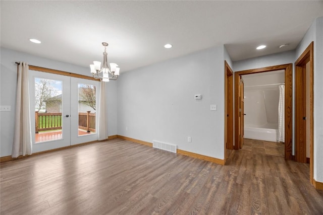 empty room with an inviting chandelier, wood finished floors, visible vents, baseboards, and recessed lighting