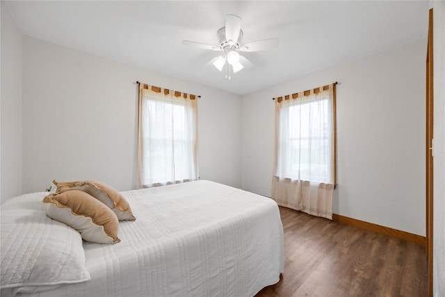 bedroom featuring baseboards, multiple windows, a ceiling fan, and wood finished floors