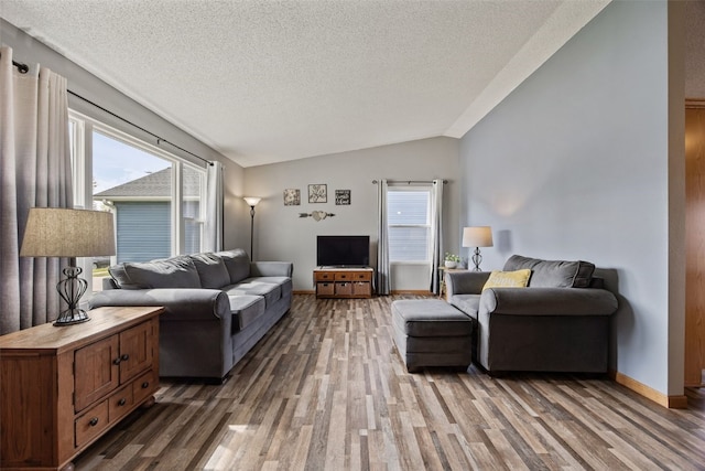 living area with a wealth of natural light, wood finished floors, lofted ceiling, and a textured ceiling