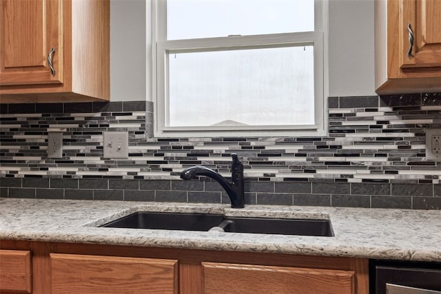 kitchen featuring brown cabinets, decorative backsplash, a sink, and light stone countertops