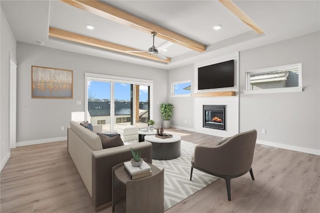 living area featuring baseboards, light wood finished floors, ceiling fan, and a large fireplace