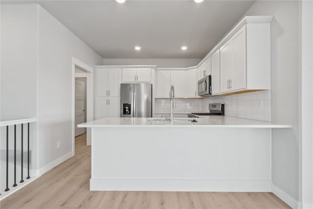 kitchen featuring a sink, stainless steel appliances, baseboards, and light wood-style floors