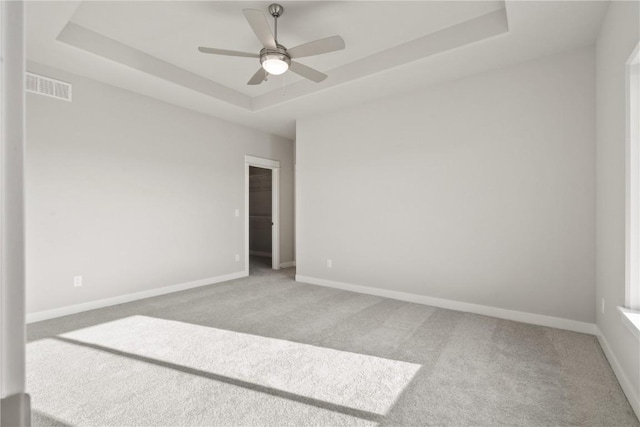 empty room featuring carpet flooring, a ceiling fan, a tray ceiling, visible vents, and baseboards