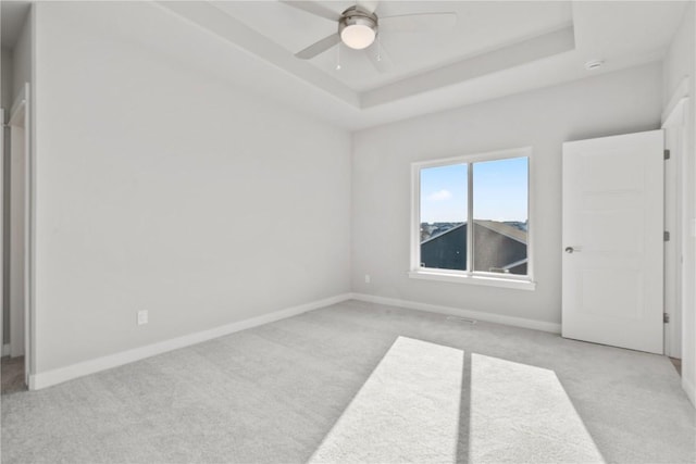 unfurnished room with light colored carpet, baseboards, ceiling fan, and a tray ceiling