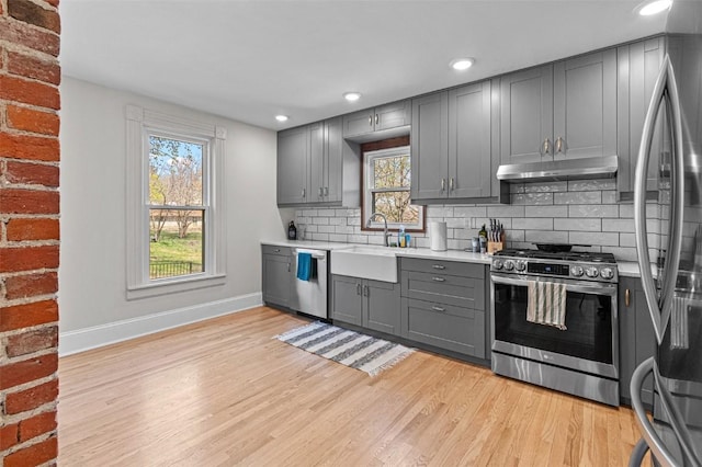 kitchen with light wood-style floors, gray cabinets, baseboards, under cabinet range hood, and appliances with stainless steel finishes