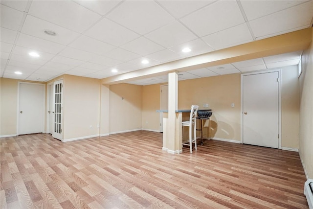 finished basement featuring baseboards, a drop ceiling, baseboard heating, and light wood-type flooring