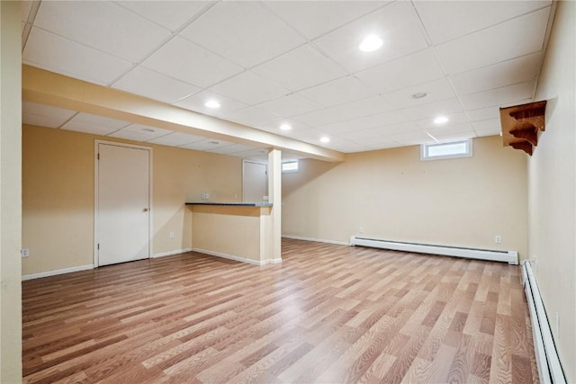basement with a baseboard radiator, baseboards, light wood finished floors, and a drop ceiling