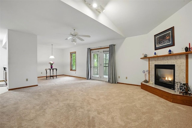 unfurnished living room featuring lofted ceiling, ceiling fan, light carpet, baseboards, and a tiled fireplace