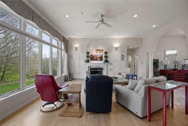 living room with a wealth of natural light, a fireplace, a ceiling fan, and arched walkways