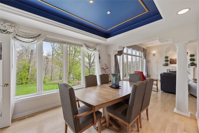dining room featuring a raised ceiling, ornate columns, light wood-style flooring, and plenty of natural light