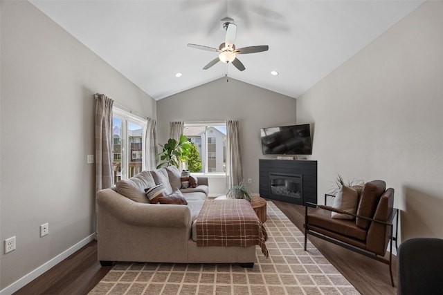living room featuring light wood-style flooring, baseboards, ceiling fan, a glass covered fireplace, and vaulted ceiling