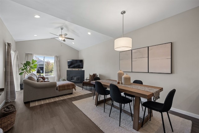 dining room featuring dark wood finished floors, baseboards, ceiling fan, a glass covered fireplace, and vaulted ceiling