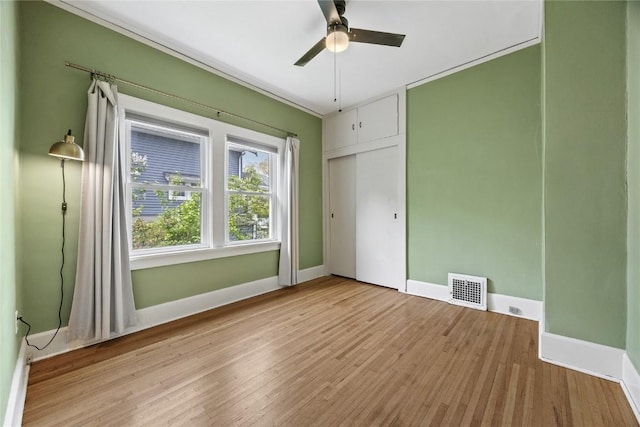 unfurnished bedroom featuring a ceiling fan, visible vents, wood finished floors, and baseboards