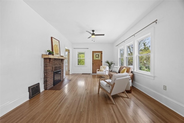 living room with a fireplace, ceiling fan, baseboards, and wood finished floors