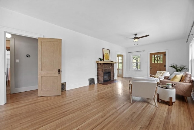 living area featuring light wood-style flooring, baseboards, ceiling fan, visible vents, and a fireplace