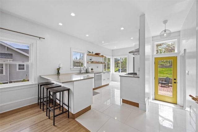 kitchen with a sink, a peninsula, dishwasher, a kitchen bar, and baseboards