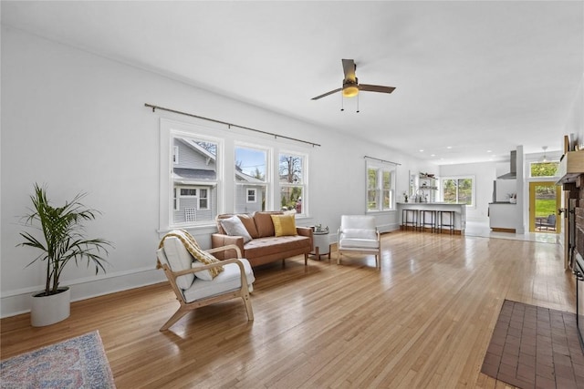 living area with a ceiling fan, baseboards, light wood-type flooring, and plenty of natural light