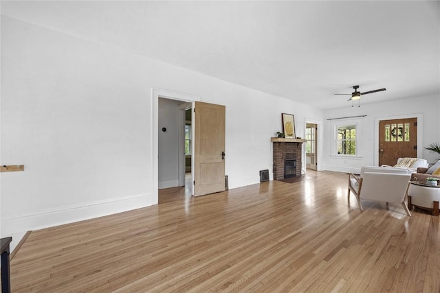 living area featuring a fireplace, ceiling fan, baseboards, and light wood-style floors