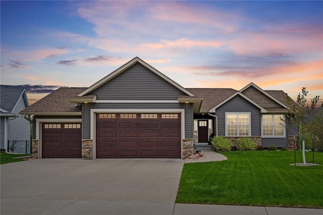 view of front facade featuring stone siding, a yard, driveway, and a garage