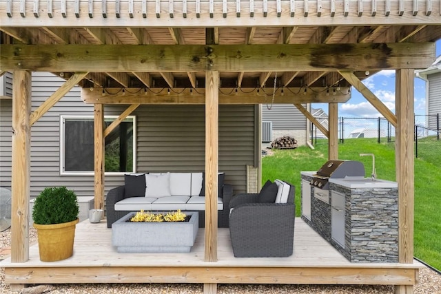 wooden deck with an outdoor living space with a fire pit, fence, a lawn, and exterior kitchen