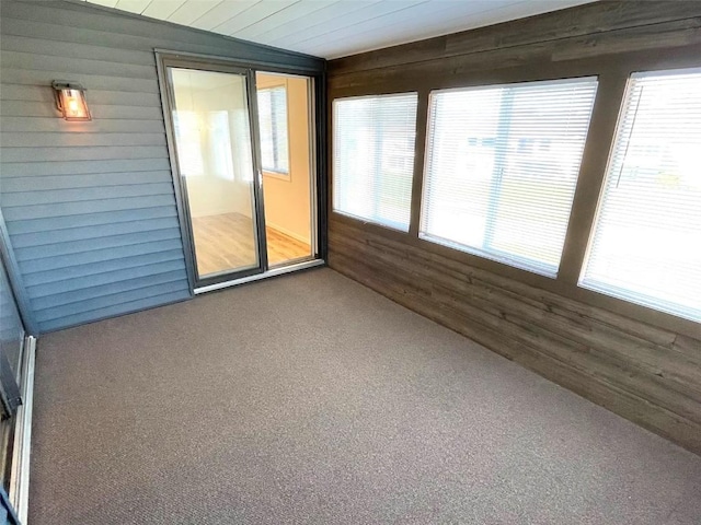 unfurnished sunroom featuring wooden walls, a healthy amount of sunlight, and carpet floors