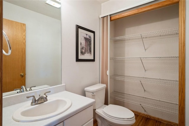 full bath with toilet, a spacious closet, vanity, and wood finished floors