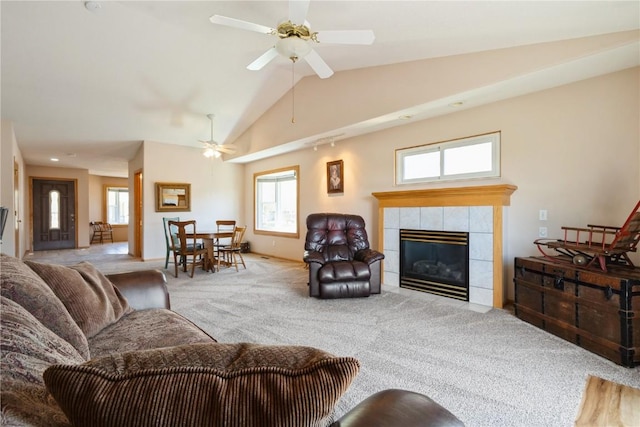 carpeted living room with lofted ceiling, baseboards, a tiled fireplace, and a ceiling fan