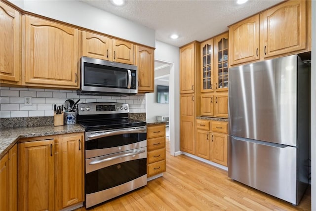 335 Parkland Dr SE, Cedar Rapids, IA 52403 - kitchen featuring glass insert cabinets, decorative backsplash, light wood-style floors, dark stone counters, and appliances with stainless steel finishes