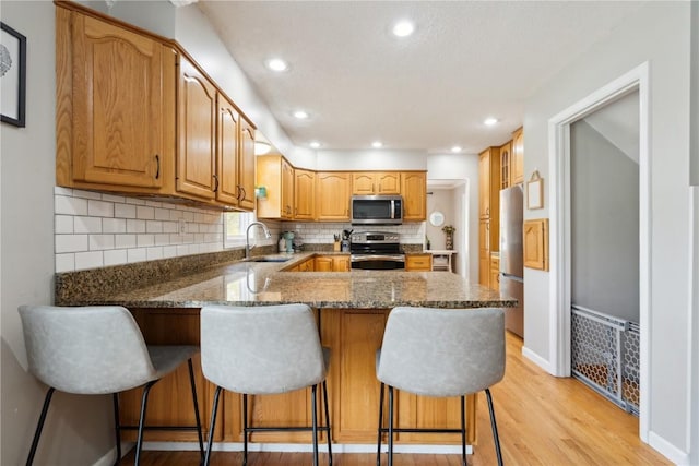 335 Parkland Dr SE, Cedar Rapids, IA 52403 - kitchen featuring a peninsula, light wood finished floors, a sink, dark stone counters, and stainless steel appliances