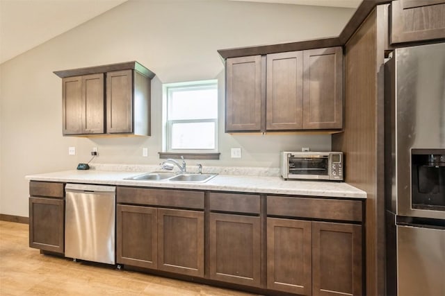 kitchen featuring appliances with stainless steel finishes, a sink, vaulted ceiling, light countertops, and light wood-type flooring