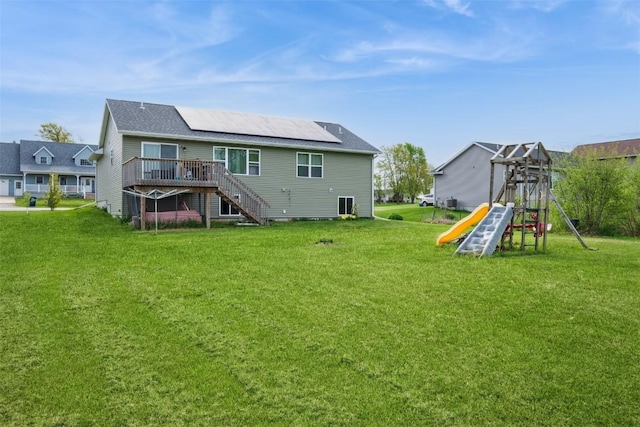 rear view of property with a playground, a yard, a wooden deck, stairway, and solar panels