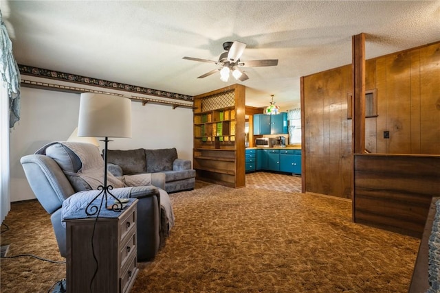 living area with dark carpet, ceiling fan, wood walls, and a textured ceiling