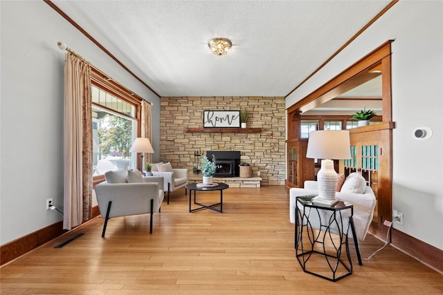 living area featuring healthy amount of natural light, light wood-style floors, a textured ceiling, a fireplace, and baseboards