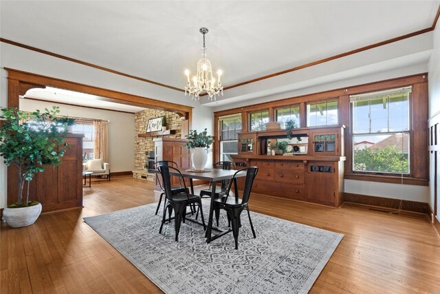 dining area featuring baseboards, a chandelier, light wood finished floors, crown molding, and a fireplace