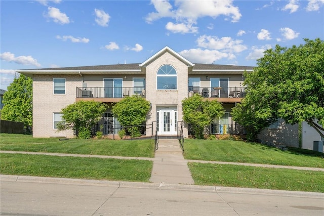 view of front of house featuring a balcony, brick siding, and a front lawn
