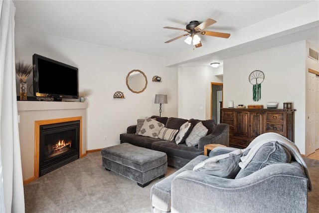 carpeted living area with ceiling fan and a lit fireplace