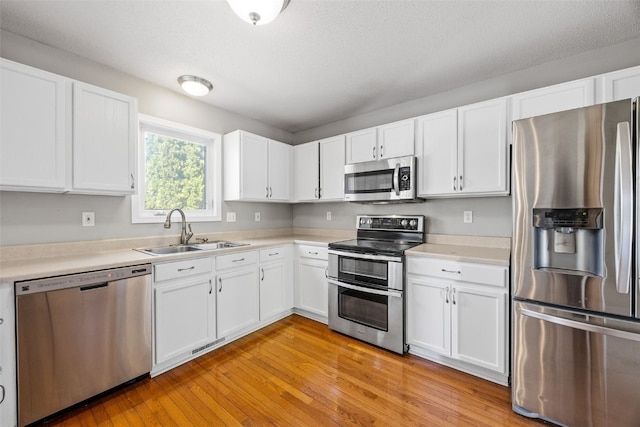 kitchen featuring appliances with stainless steel finishes, a sink, light wood finished floors, light countertops, and a textured ceiling
