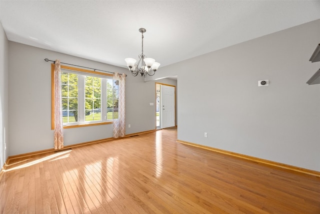 spare room featuring a chandelier, light wood-style floors, and baseboards