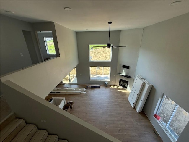 living room featuring a towering ceiling, wood finished floors, a ceiling fan, a glass covered fireplace, and stairway