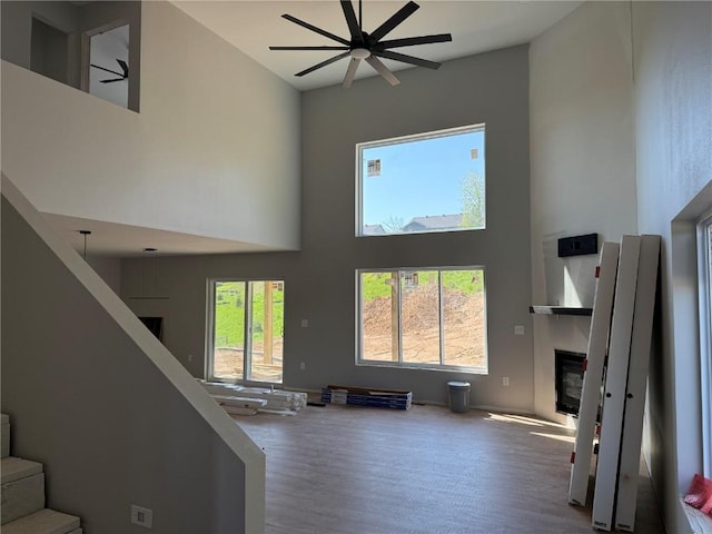 living room featuring a ceiling fan, a high ceiling, stairs, a glass covered fireplace, and wood finished floors