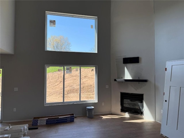 unfurnished living room featuring a glass covered fireplace, wood finished floors, a towering ceiling, and baseboards