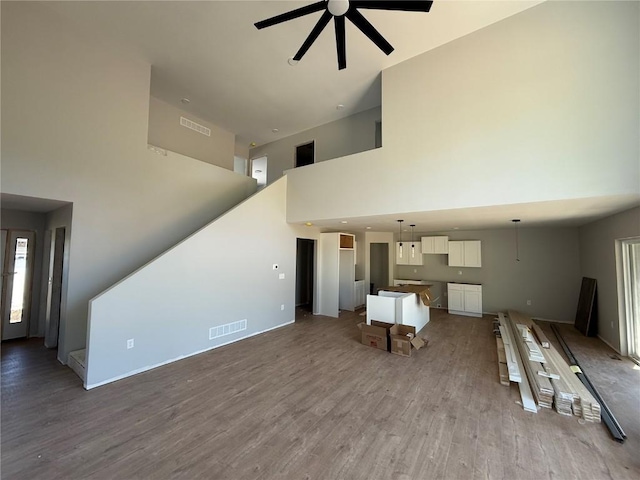 unfurnished living room featuring a ceiling fan, a towering ceiling, wood finished floors, and baseboards