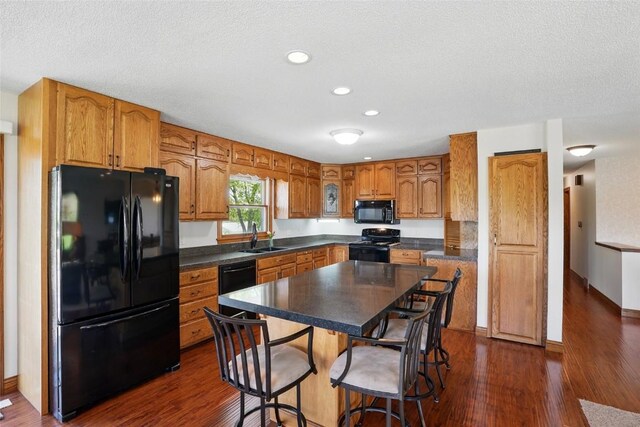 kitchen with black appliances, a sink, brown cabinetry, dark wood-type flooring, and recessed lighting