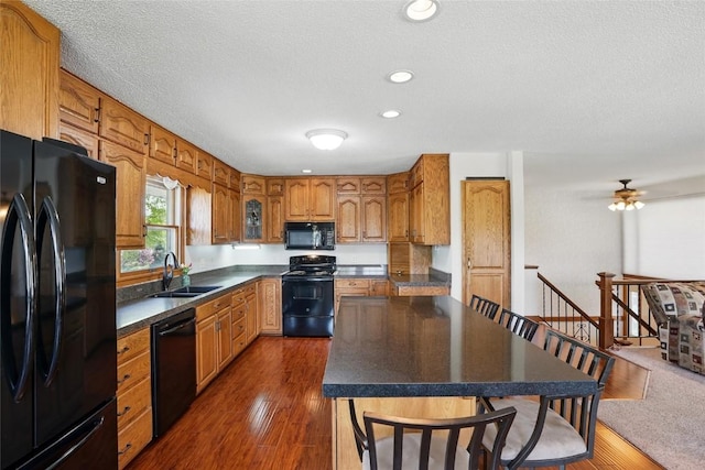 kitchen with black appliances, a sink, dark countertops, brown cabinetry, and a kitchen island
