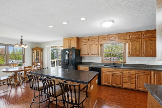 kitchen featuring black appliances, a sink, dark countertops, a breakfast bar, and a chandelier