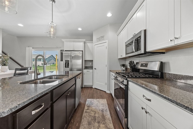 kitchen featuring appliances with stainless steel finishes, a sink, dark wood-style floors, white cabinetry, and pendant lighting